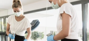 woman-with-gloves-medical-mask-disinfecting-weights-gym